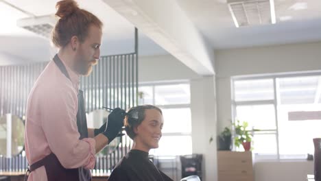 caucasian male hairdresser dyeing happy female client's hair at salon, copy space, in slow motion