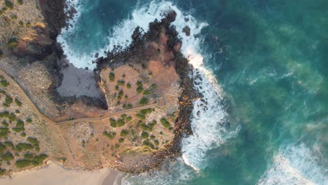 Top-aerial-view-over-sea-waves-splashing-to-the-coastline-shores,-location-recorded-at-Bordeira,-Portugal