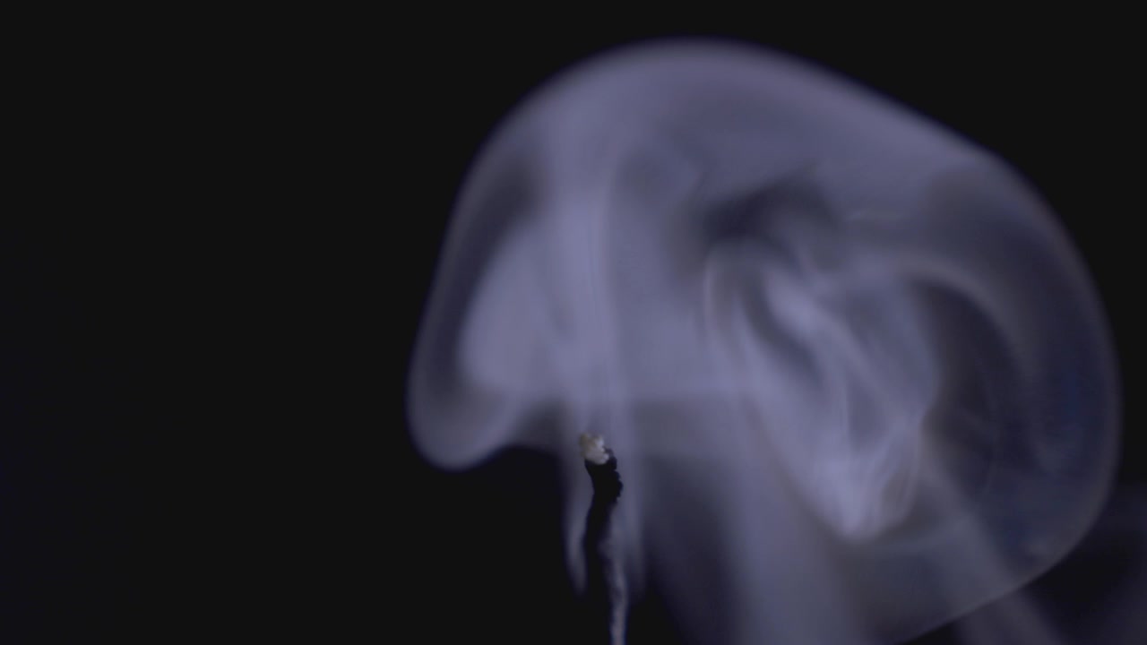 Candle Glowing In Dark Background Just Been Blown Out With Smoke Trail. - close up shot