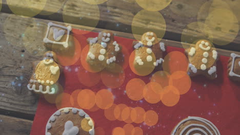 animation of yellow and orange light spots over christmas gingerbread men and decorated cookies