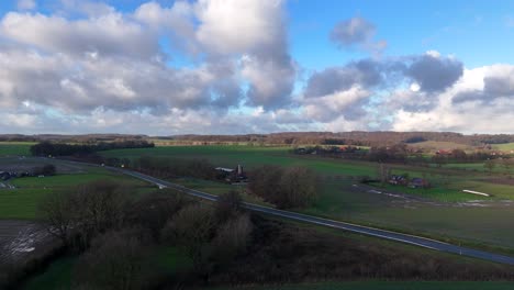 Aerial establishing shot of cars on intersection in american countryside. Sunny winter day with clouds at sky. Rural countryside farmsteads with silos. Wide shot.