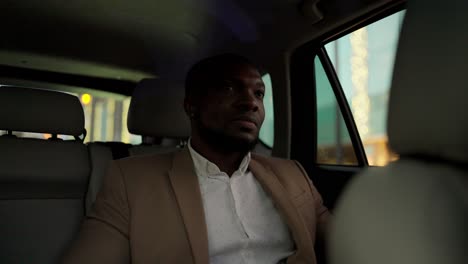 a man with black skin and a beard in a brown suit waits for the driver to start moving while sitting in a modern car interior and looking out the window