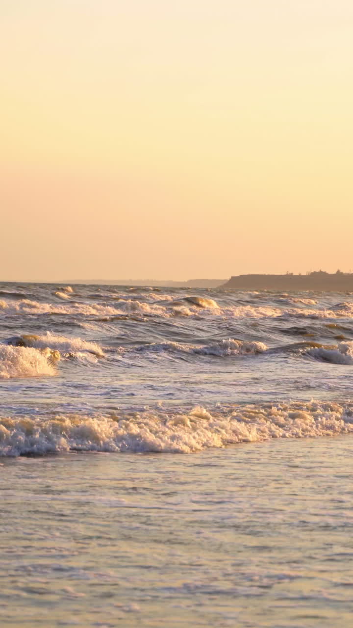 White sea foam covers the sandy coast at sunset. Foaming sea wave washes sandy shoreline on beautiful summer evening Vertical video