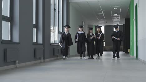 grupo de felices estudiantes de preescolar multirraciales con birrete y bata. están corriendo y sosteniendo diplomas.