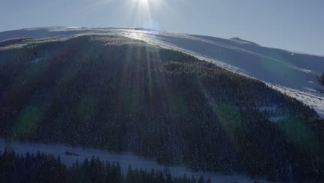 sun flare with rainbow rays across a snow laden mountain full of pine trees.