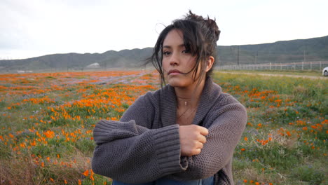 a beautiful girl with black hair looking sad and depressed in a rural field of wild flowers blooming in springtime slow motion