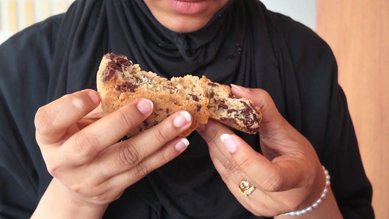 Mulher Quebrando um Cookie Fresco com Gotas de Chocolate ao Meio