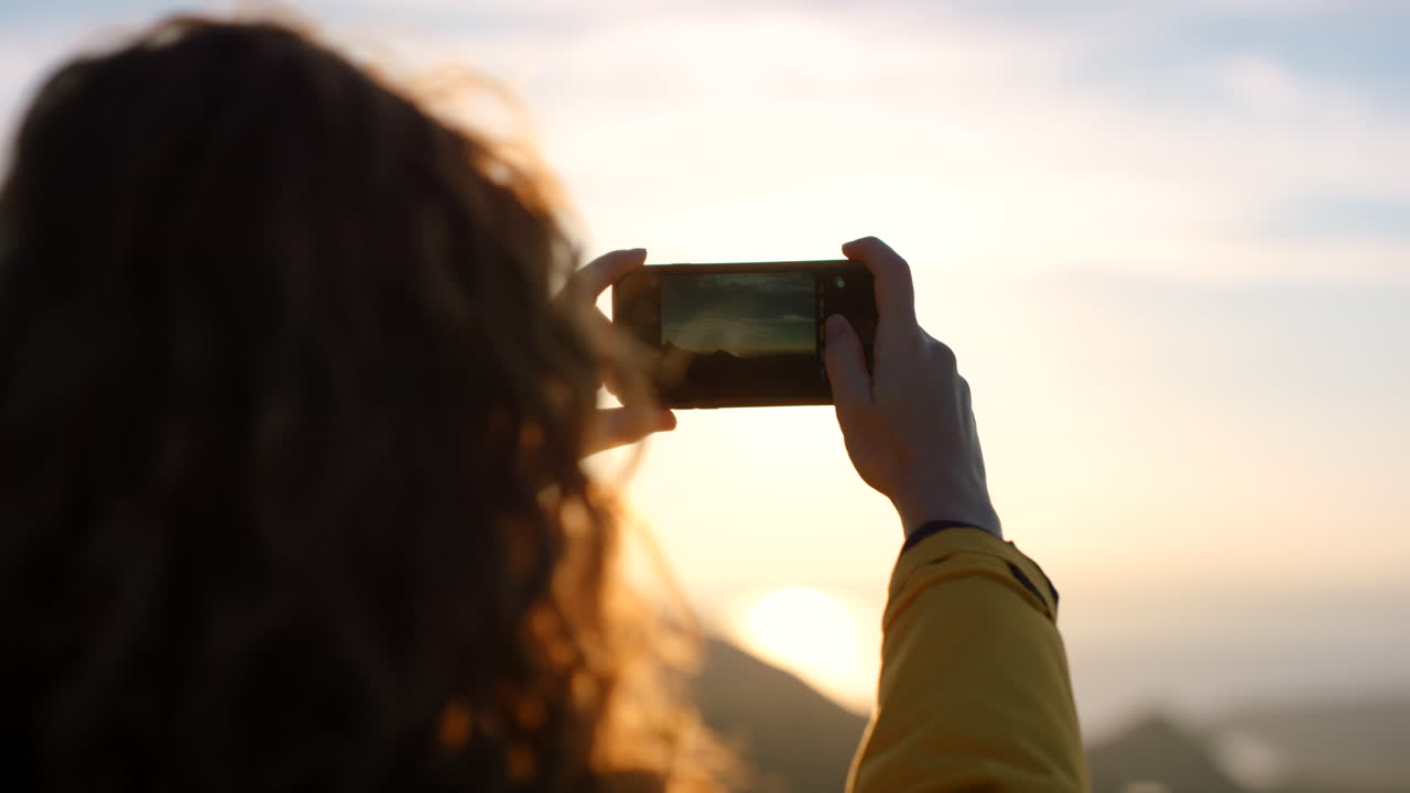mujer tomando una foto de la puesta de sol desde una montaña