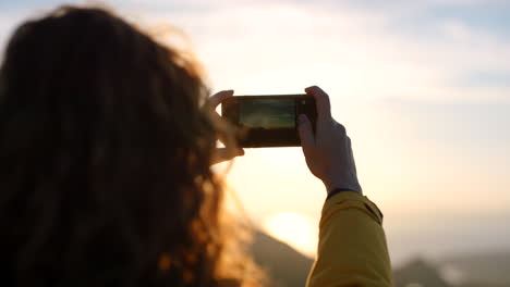 woman taking photo of sunset from a mountain