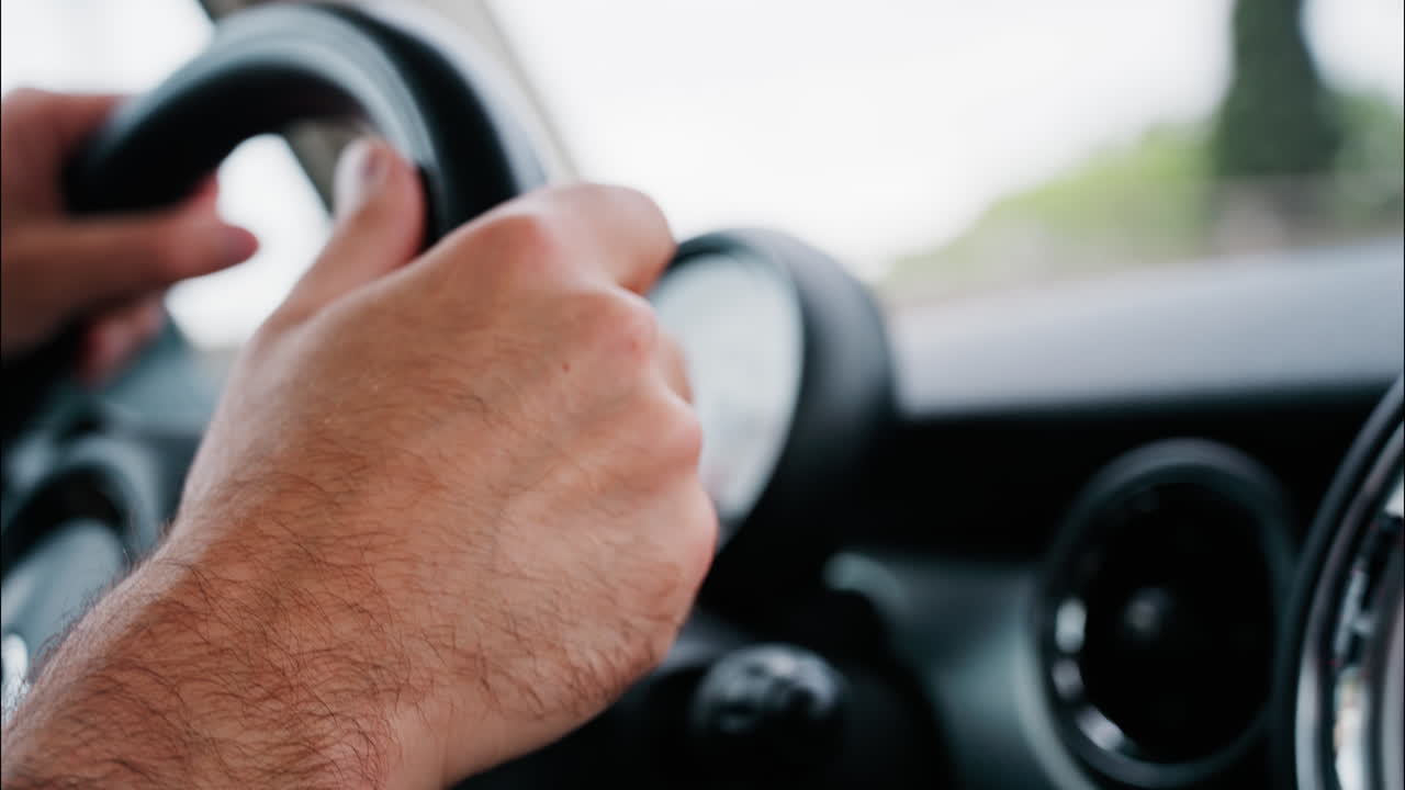 Close up of a man's hands on a steering wheel, driving a car on the road