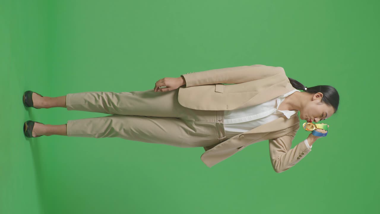 옷을 입은 아시아 사업가 여성이 손에 금메달을  자부심을 느끼며 스튜디오의 녹색 스크린 배경에서 첫 번째 우승자로 승리합니다.