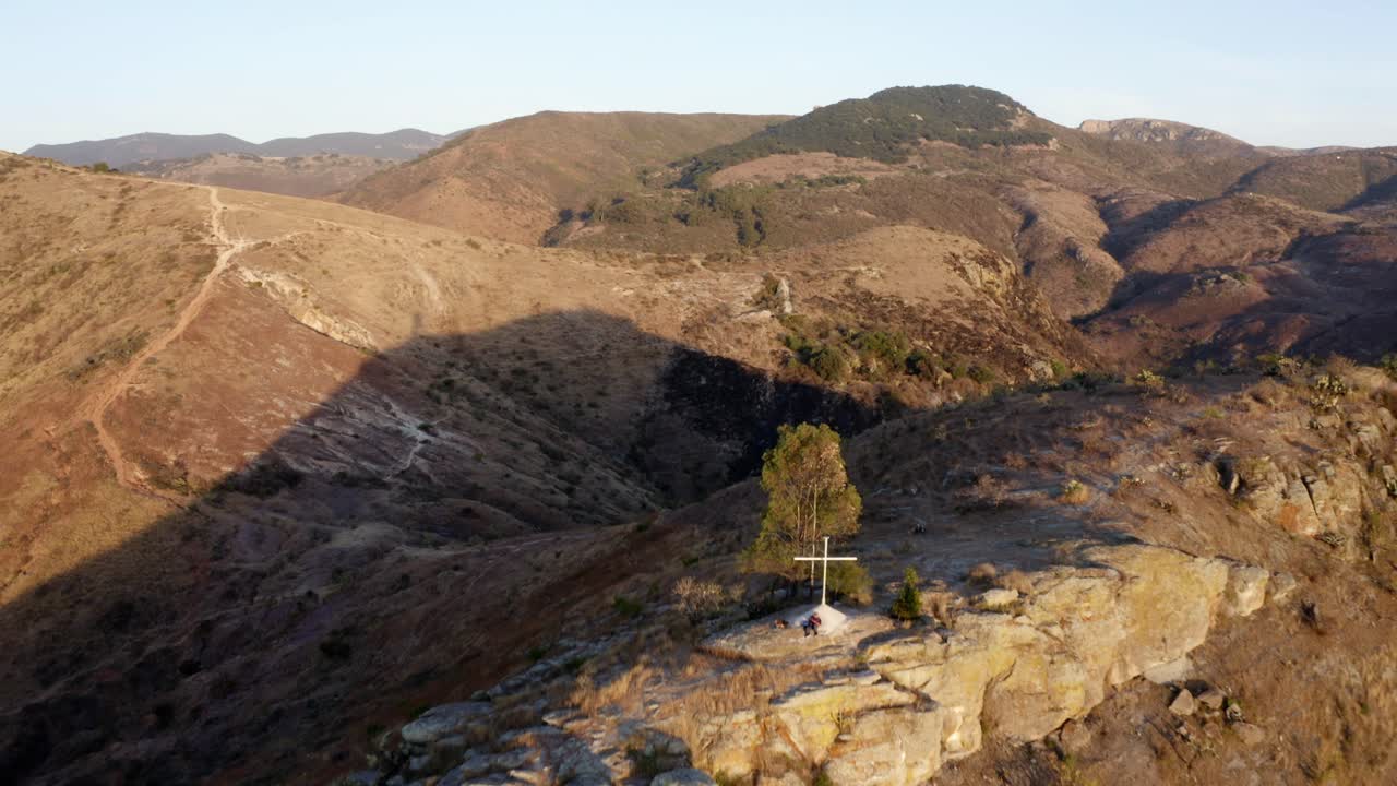 저녁 시간 동안 언덕이 많은 지형 꼭대기에 있는 기독교 무덤의 공중 후방 이동 샷