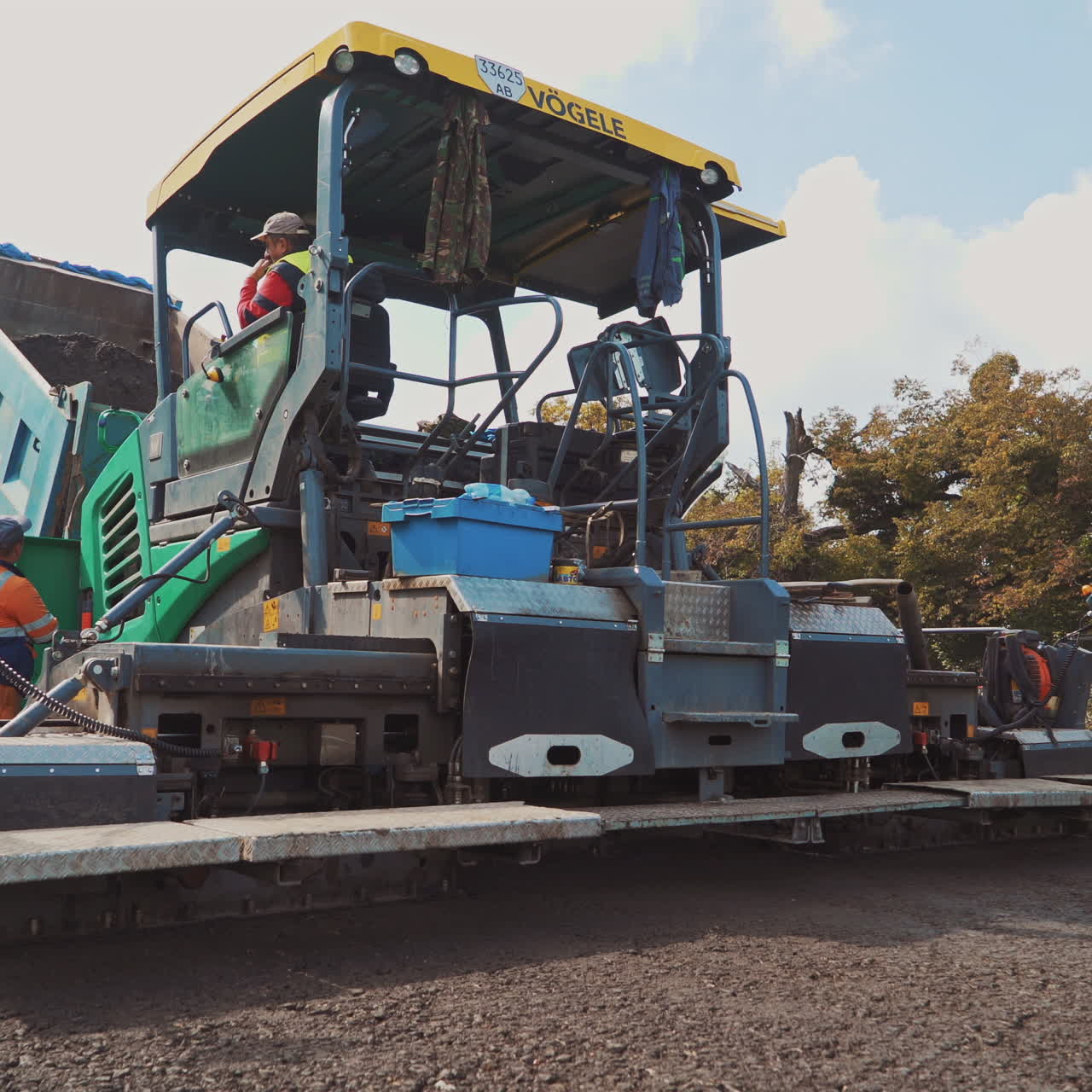 Large asphalt laying machine and team of workers on the road. Asphalt spreader at work in summer. Process of road construction.