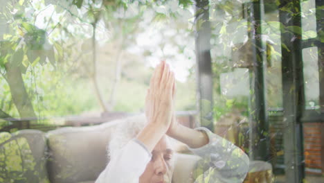 animation of leaves over senior caucasian woman practicing yoga and meditating