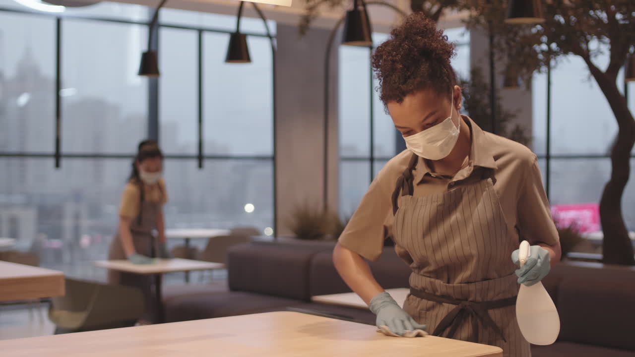 Female Cafe Worker Disinfecting Table