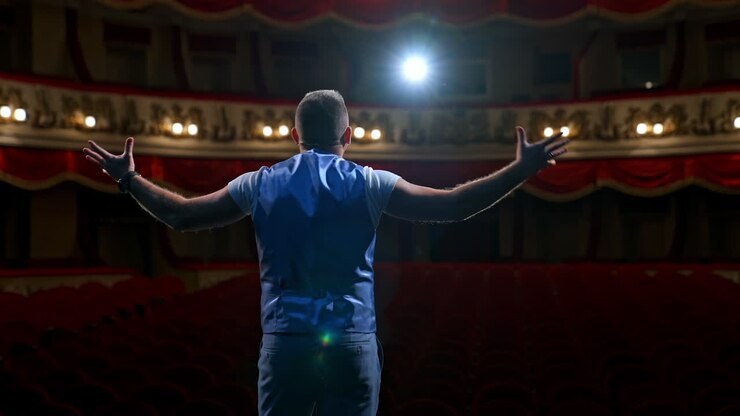 Middle age male entertainer, presenter or actor on stage. Public speaker gives performance in front of empty auditorium. Man in theater.