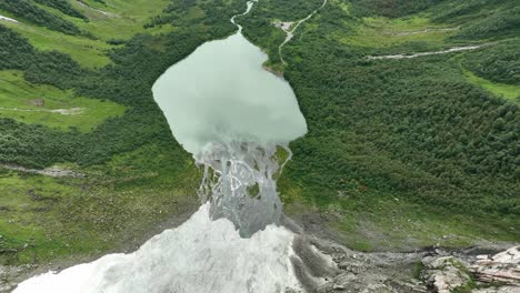 Glacier-runoff-water-from-Boyabreen-glacier-to-glacial-lake-Brevatnet-in-Fjaerland-Norway---Aerial-moving-down-from-glacier-towards-green-lake-and-valley