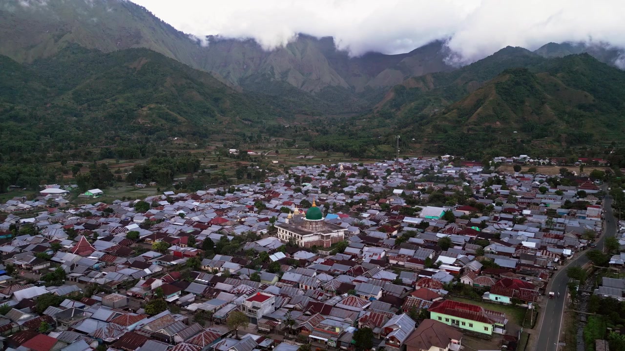中央にモスクがあり、肥沃な谷、農地、そびえ立つ緑の山々に囲まれた密集した住宅街が広がる山間の町、プッシュイン空撮ドローン映像