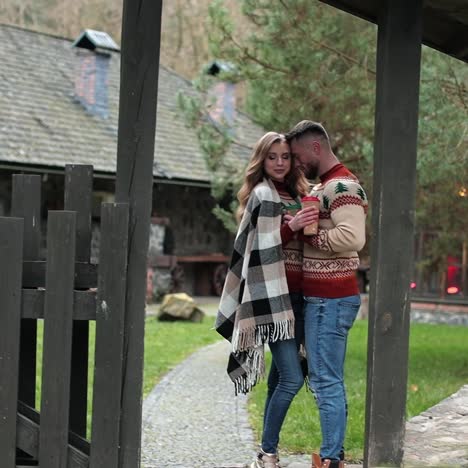 couple in love standing at the gates of a rural complex. happy couple hugging near the country house gates. pair in warm sweaters enjoying autumn in the village