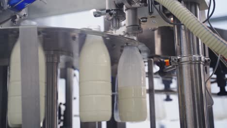 Upgraded technology in dairy factory. Plastic bottles filling with milk by mechanical machine. Process of pouring milk into plastic bottles moving in a circle. Dairy production.