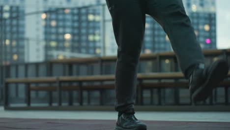 Leg view of athlete skillfully juggling football on sport arena, highlighting precise ball control, concentration, and athletic prowess against urban backdrop with benches and illuminated pathways