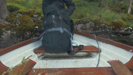 el joven pone la mochila en la proa del barco y se sube