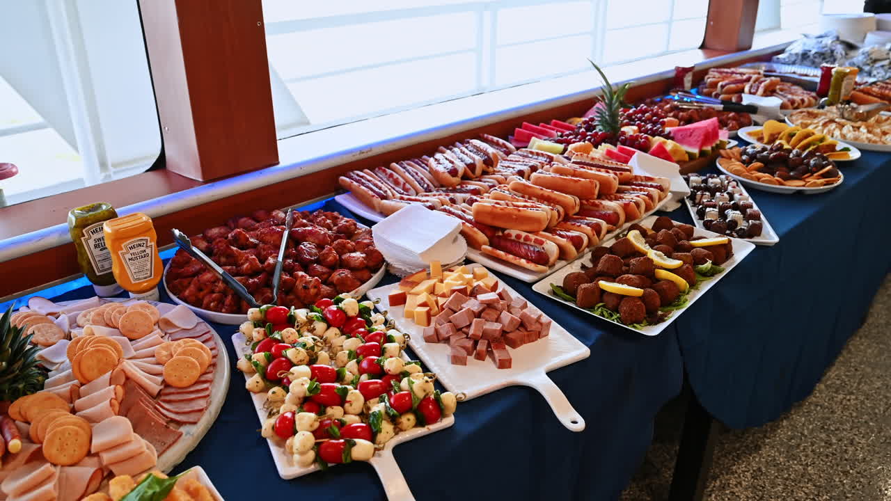 New York, USA, 1° agosto 2025: elegante buffet con vassoi di carne, formaggio e frutta. Tavolo da buffet di lusso su una nave con prosciutto, alette di pollo, hot dog e vassoi di frutta fresca disposti per gli ospiti