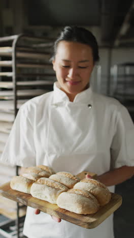 vertical video of portrait of happy asian female baker with bread in bakery
