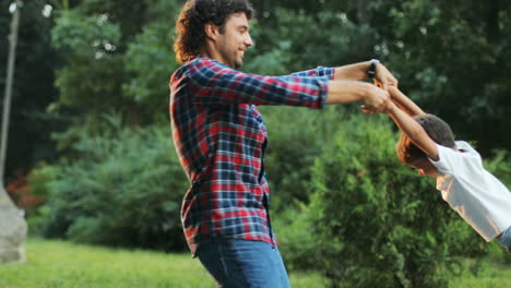 Portrait-of-a-young-father-and-his-little-son.-They-are-playing-on-the-backyard.-Dad-is-spinning-the-boy.-Blurred-background