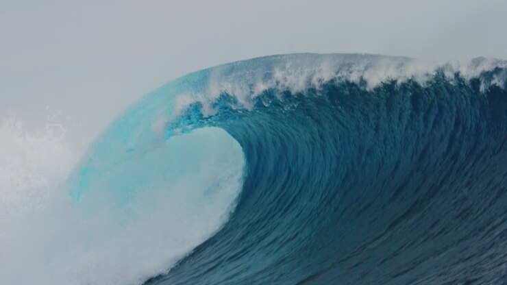 Perfect empty blue barreling wave with spitting whitewash and heavy lip, water sparkles from sunlight