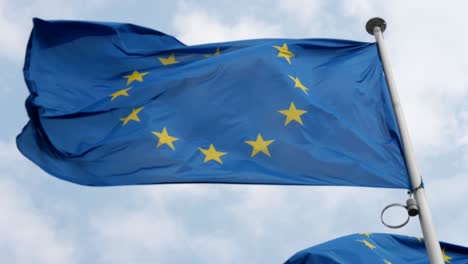 vista de abajo de la bandera de la unión europea ondeando orgullosamente en el aire en un día soleado de verano. el cielo es celeste y nublado.