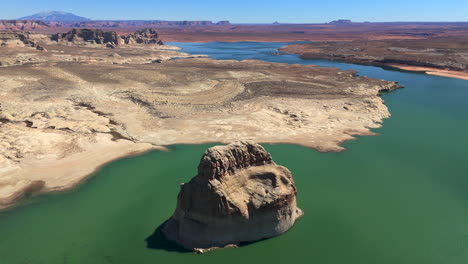 lone rock in green waters of lake powell at glen canyon national recreation area, utah. aerial pullback shot