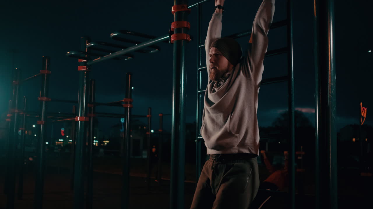 hombre realizando pull-ups en un parque de entrenamiento en la calle por la noche