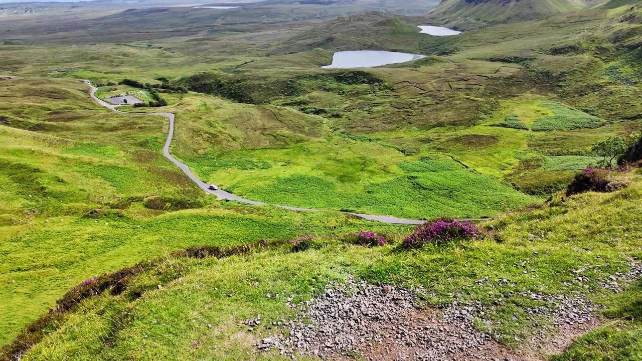 Vista dall'alto di un'auto che percorre una strada in una splendida valle verde vicino al monte Quiraing sull'Isola di Skye, Scozia, in una giornata estiva e soleggiata.