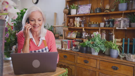 female owner of florists shop with laptop talking on mobile phone