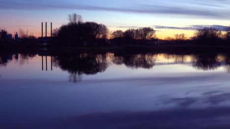 Slow-pan-across-a-beautiful-sunset-over-a-lake-with-the-smokestacks-of-industry-background