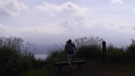 male hiker climbing on top of bench close to mt fuji looking into distance