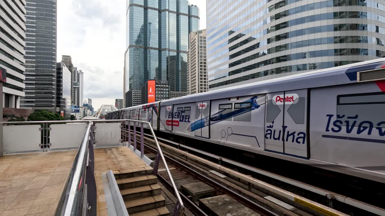 Modern skytrain approaches elevated station in Bangkok, daylight, wide shot, urban cityscape, static camera