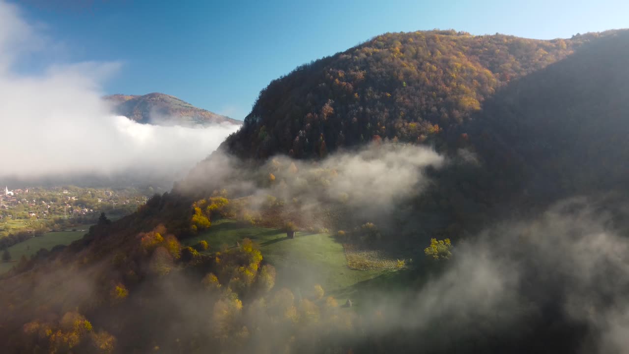 remota cabaña de madera tradicional vista desde el cielo, hermosas nubes cubriendo los colores de finales de otoño de las montañas en transilvania, rumania