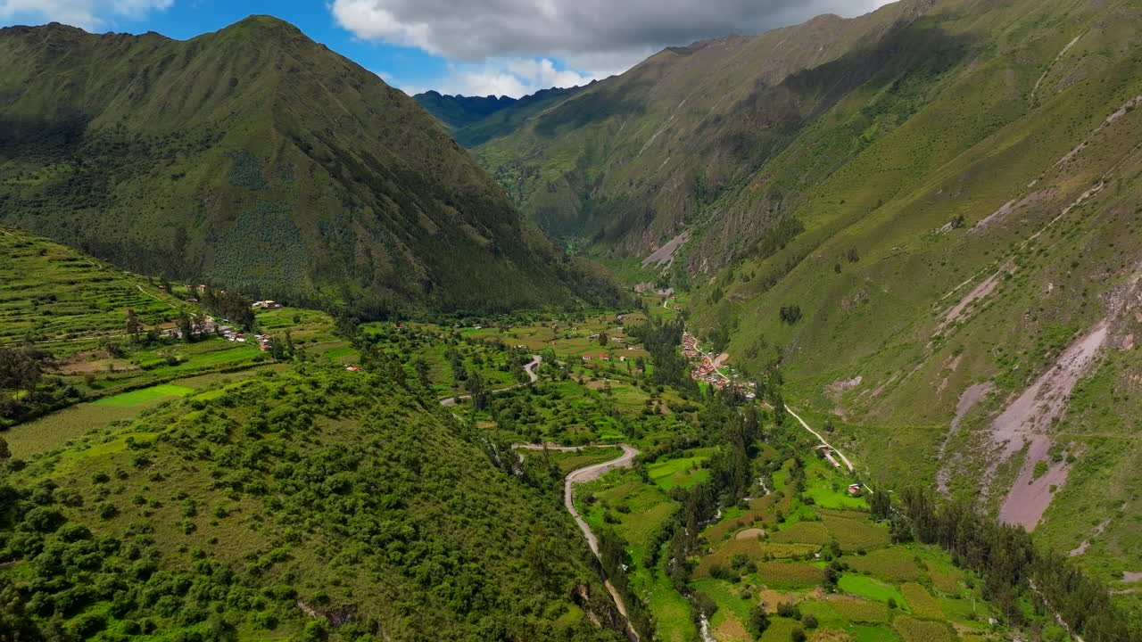 Planata aerea sopra una valle montana verde con campi e una strada rurale tortuosa vicino a Ollantaytambo, Perù, ideale per progetti di viaggio, natura, destinazioni e paesaggi.
