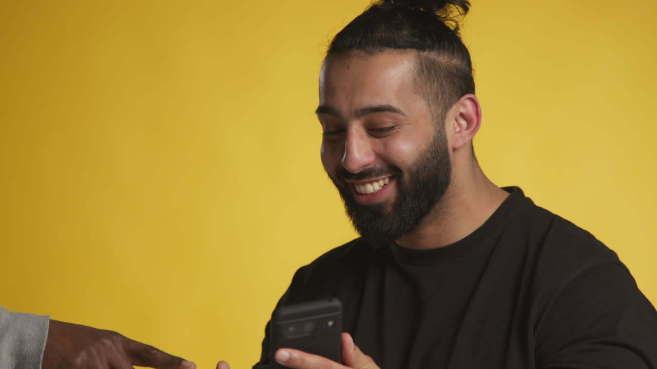 Studio Shot Of Two Excited Male Friends With Mobile Phone Celebrating Winning Money Against Yellow Background