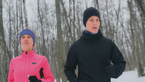 positives schönes junges gesundes paar, das am sonnigen wintermorgen mit sportkleidung durch den wald läuft.