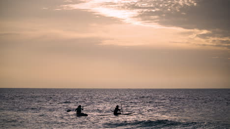 Two-Young-Women-Stand-Up-Paddle-Boarding-in-Hawaii-at-Sunset-on-Their-SUPs---scenic-colorful-sundown-over-sea