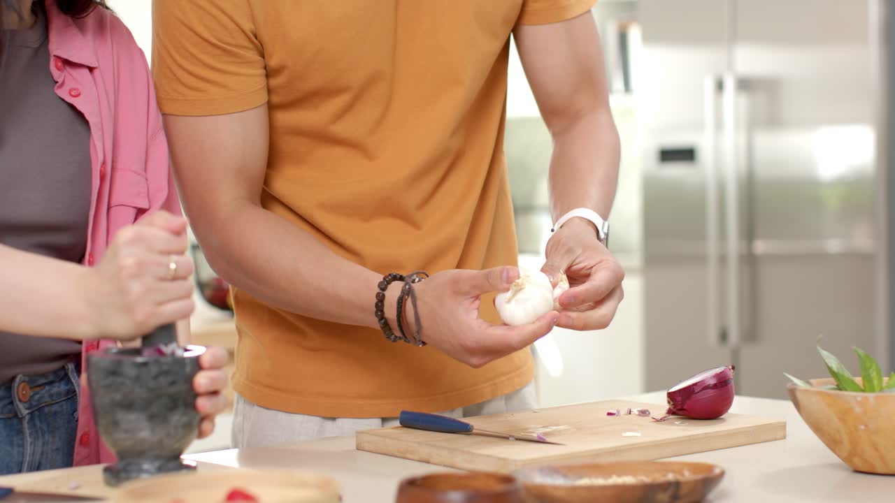 Verschiedenes Paar mahlt mit Mörser und Stößel und schält Knoblauch an der Küchentheke für das Abendessen