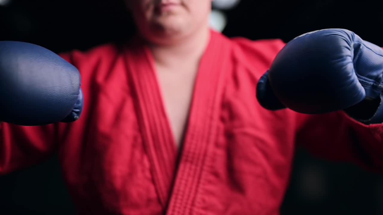 Taekwondo practitioner in a red kimono and gloves is boxing in front of him in a gym. Slow motion