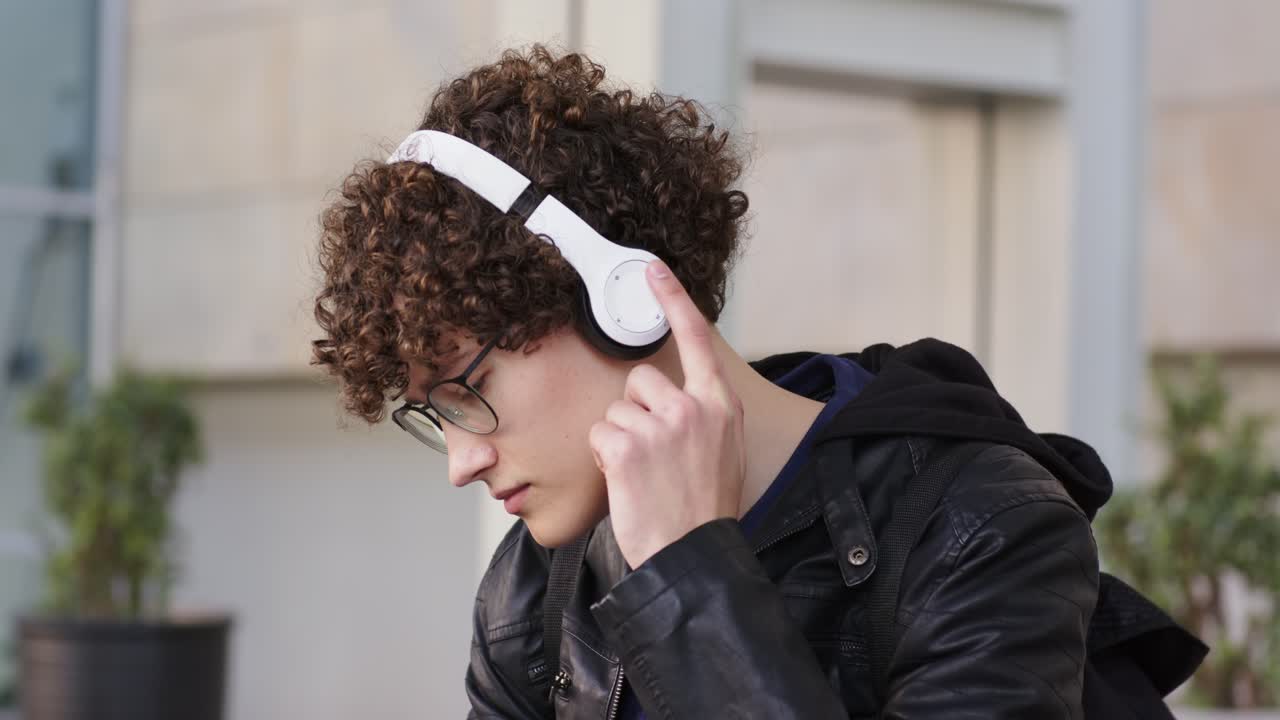 Studente seduto su una panchina della piazza che tira fuori le cuffie dallo zaino, annuisce a tempo di musica, spazio per il testo