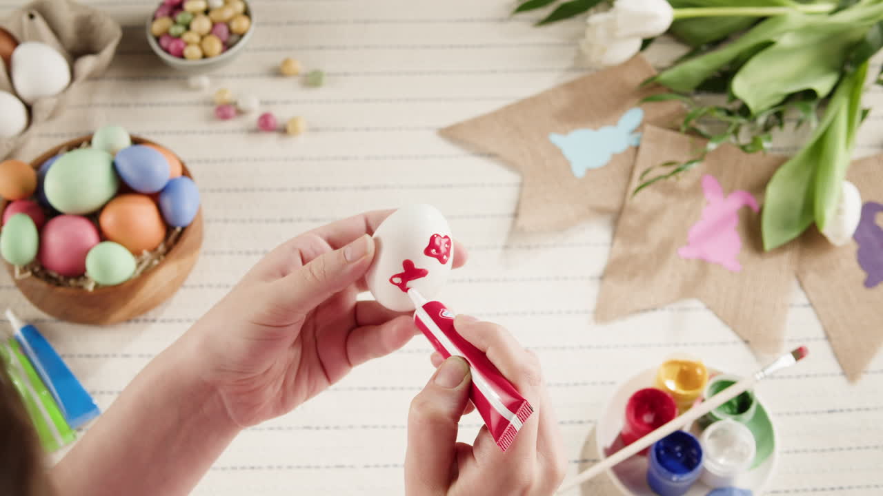 Primo piano di mani che decorano un uovo di Pasqua con pittura rossa