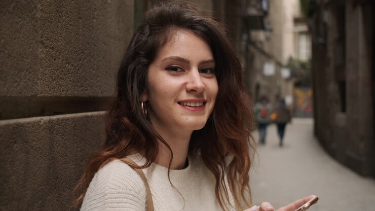 Mujer mirando a cámara mientras sostiene el teléfono móvil.