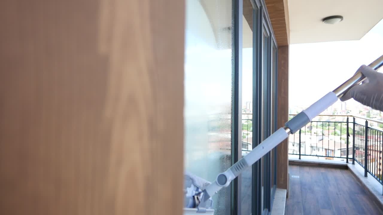 Eine Frau putzt ein Fenster auf einem Balkon mit Stadtblick