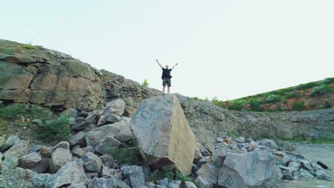 Tourist man standing on a big rock and raises his hands up on the stones background under the clear sky. Happy young hiker man tourist between the rocks outdoors.